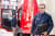 Mann mit Brille und Laptop-Tasche vor einem roten Lieferwagen, im Hintergrund eine weitere Person.